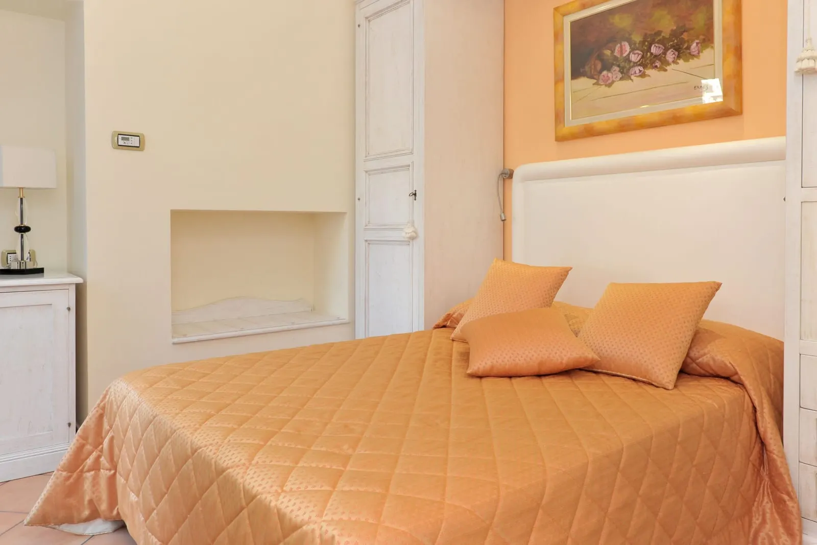 Economy Double at Hotel Santa Lucia: a bed with an orange quilted cover under a white headboard, beside a wall niche and a white wardrobe