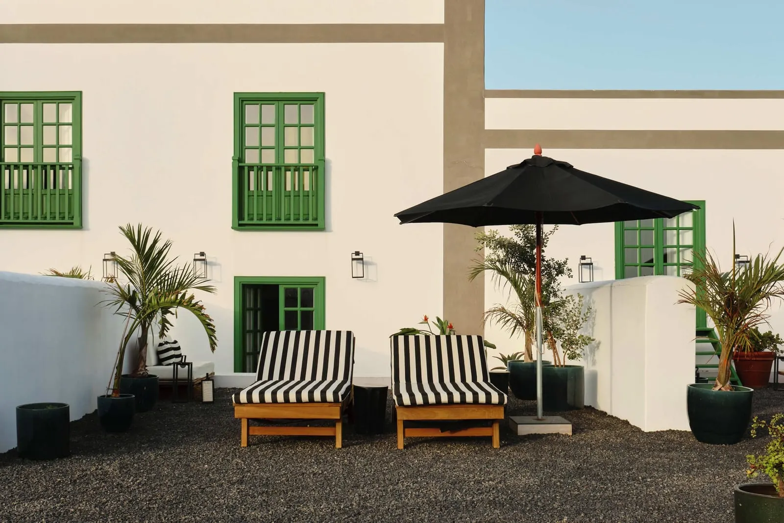Superior Room with Terrace and Sea View à l'Hotel César Lanzarote : des bains de soleil rayés et un parasol noir sur une terrasse devant des fenêtres à volets verts