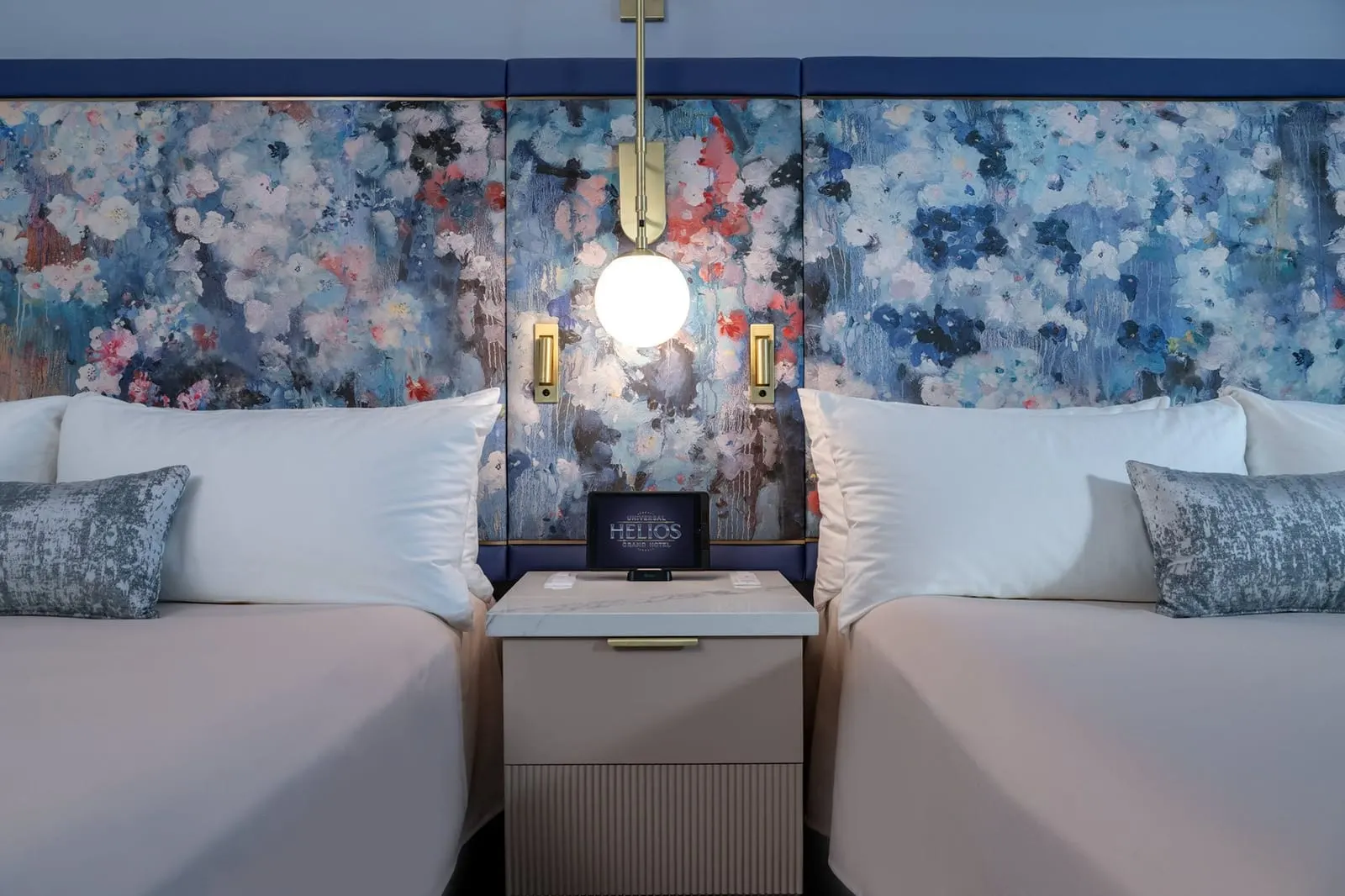 Park View 2 Queen Beds room at Universal Helios Grand Hotel: the floral upholstered headboard behind the two queen beds, with reading lights and a bedside tablet between them