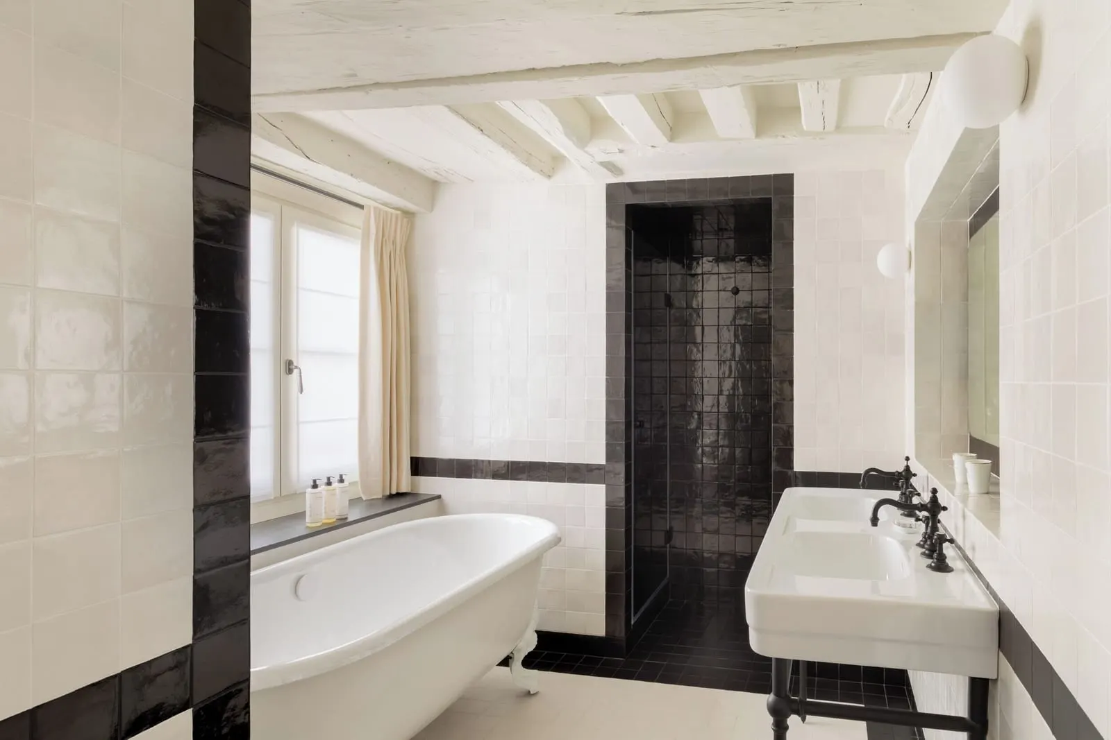 Junior Suite at Le Pavillon de la Reine: the bathroom, with a claw-foot bath, a double washbasin and a black-tiled shower under whitewashed beams