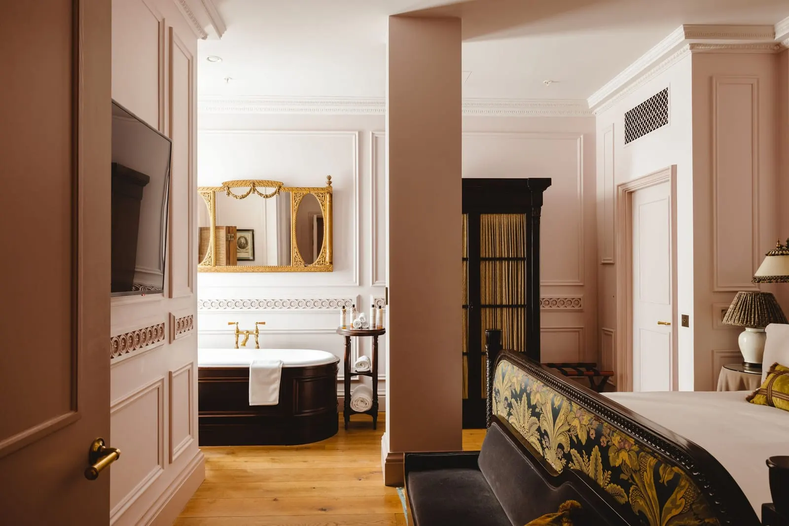 Lutyens Suite at The Ned: a bedroom with pink walls and a doorway through to a bath under a gilt mirror