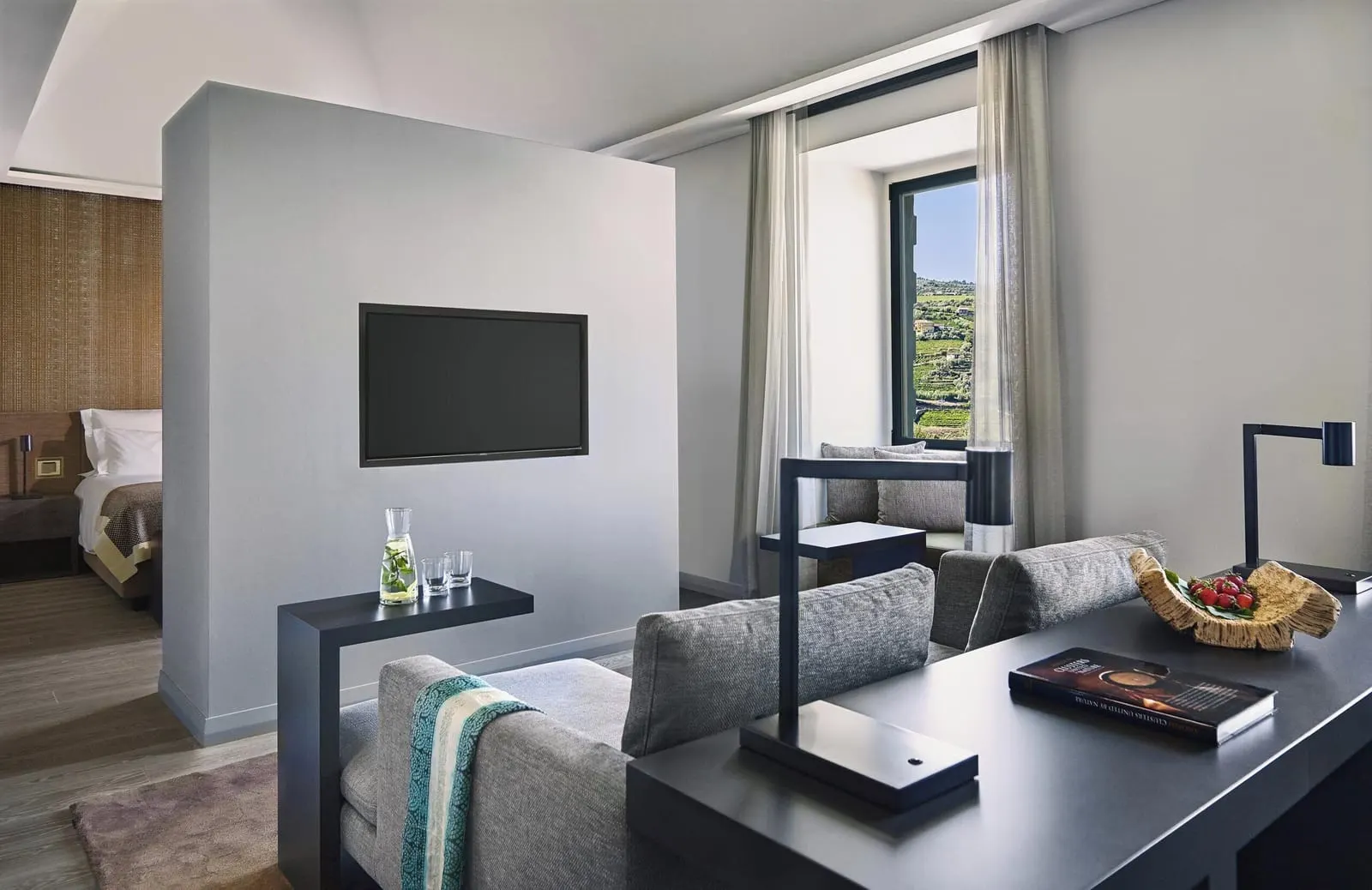 Quinta Junior Suite at Six Senses Douro Valley: a sofa and desk in the sitting area, with the bed behind a TV wall