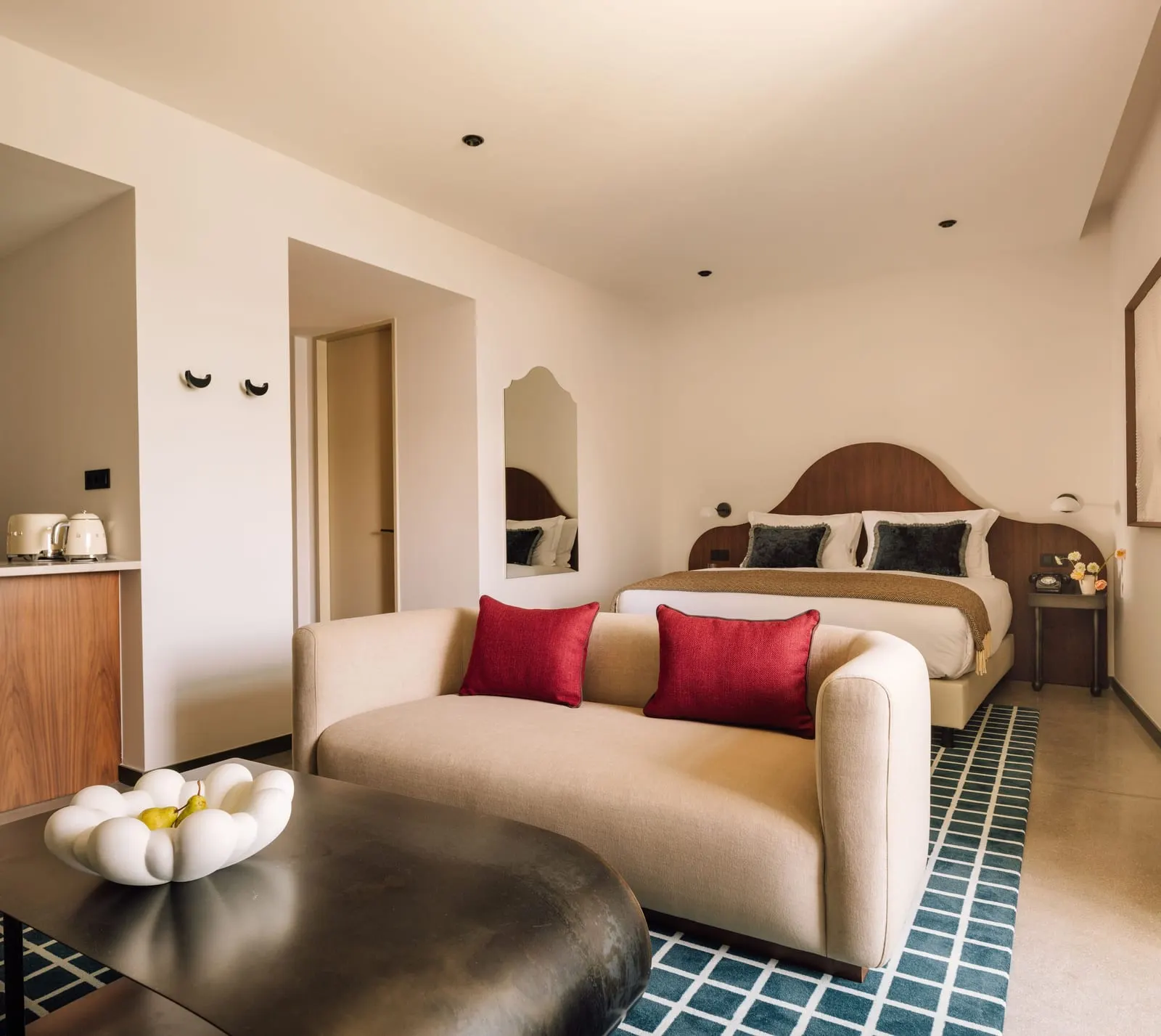 King or Queen Studio at The Rebello: the bed, a sofa with red cushions and a low table, with the kitchen on the left