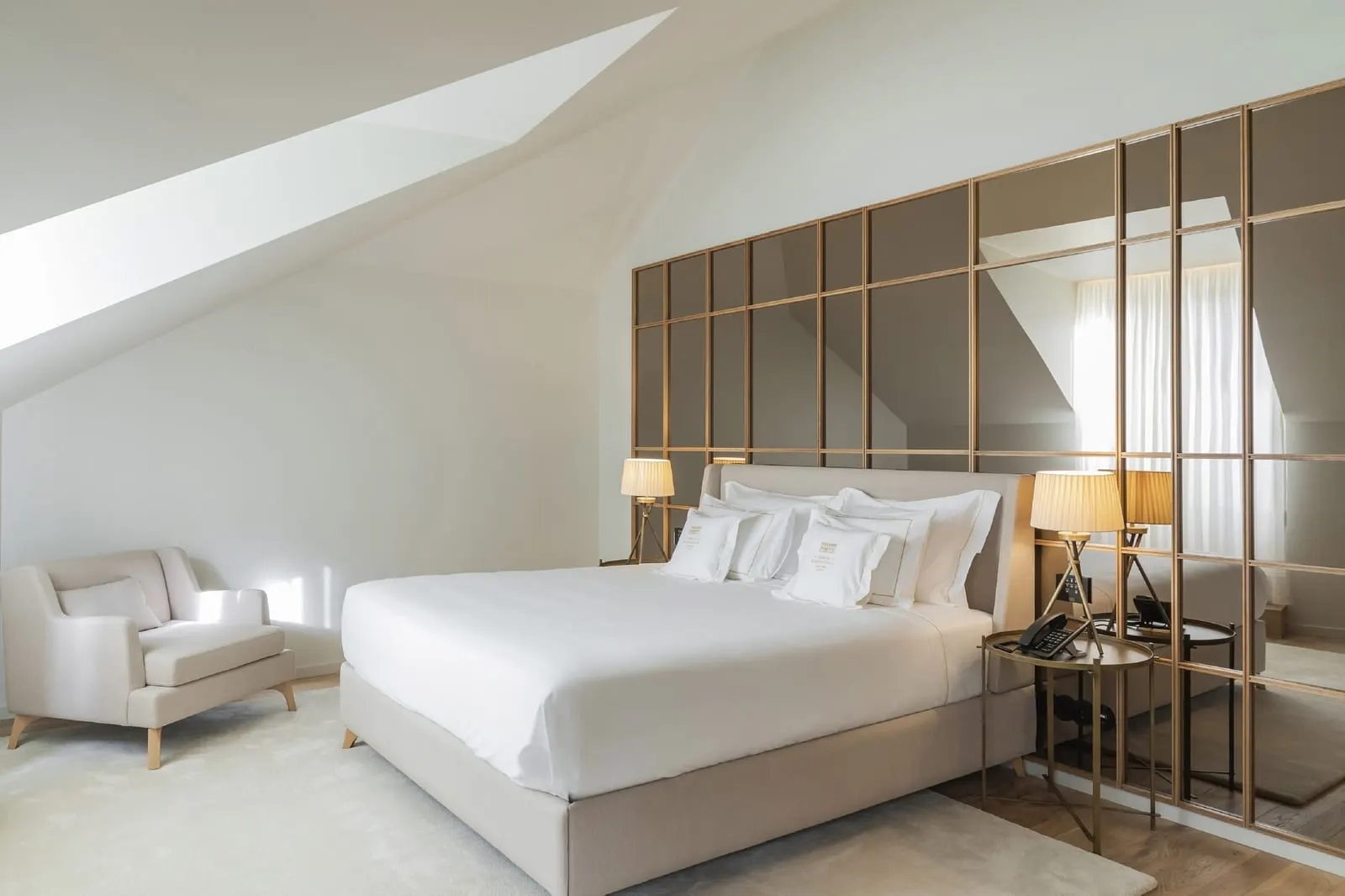 King Suite at Casa da Companhia: the bed against a brass-framed mirror wall under a sloping ceiling, with an armchair