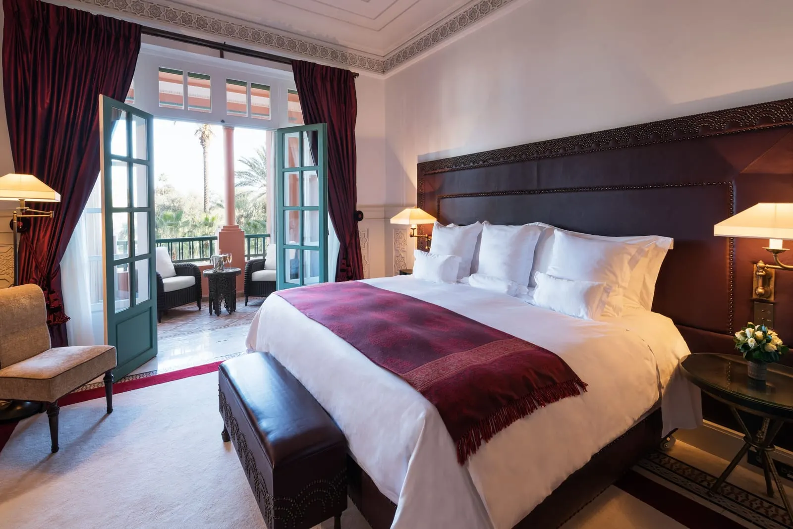 Prestige Suite at La Mamounia: a king bed with a red throw facing doors open to a balcony with armchairs