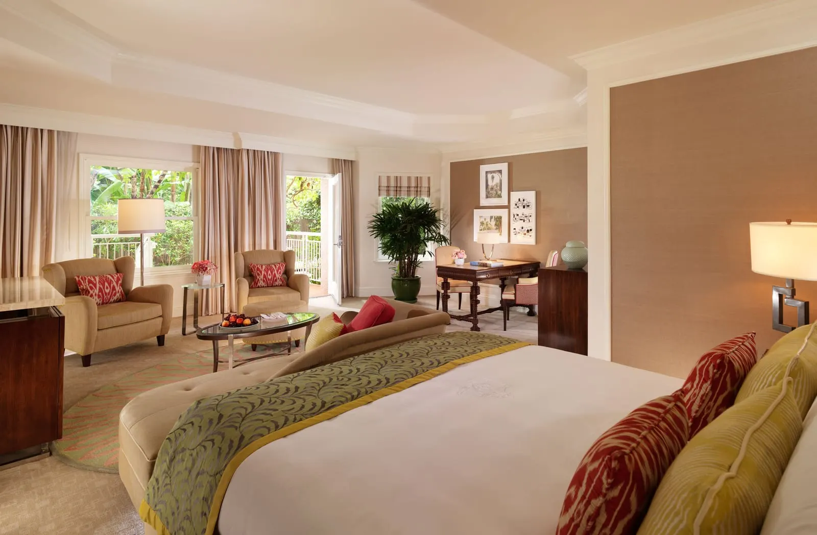 Junior Suite with Patio at The Beverly Hills Hotel: a bed with a chaise at its foot, a sitting area with two armchairs and a glass coffee table, a writing desk and an open French door to a patio with a white railing