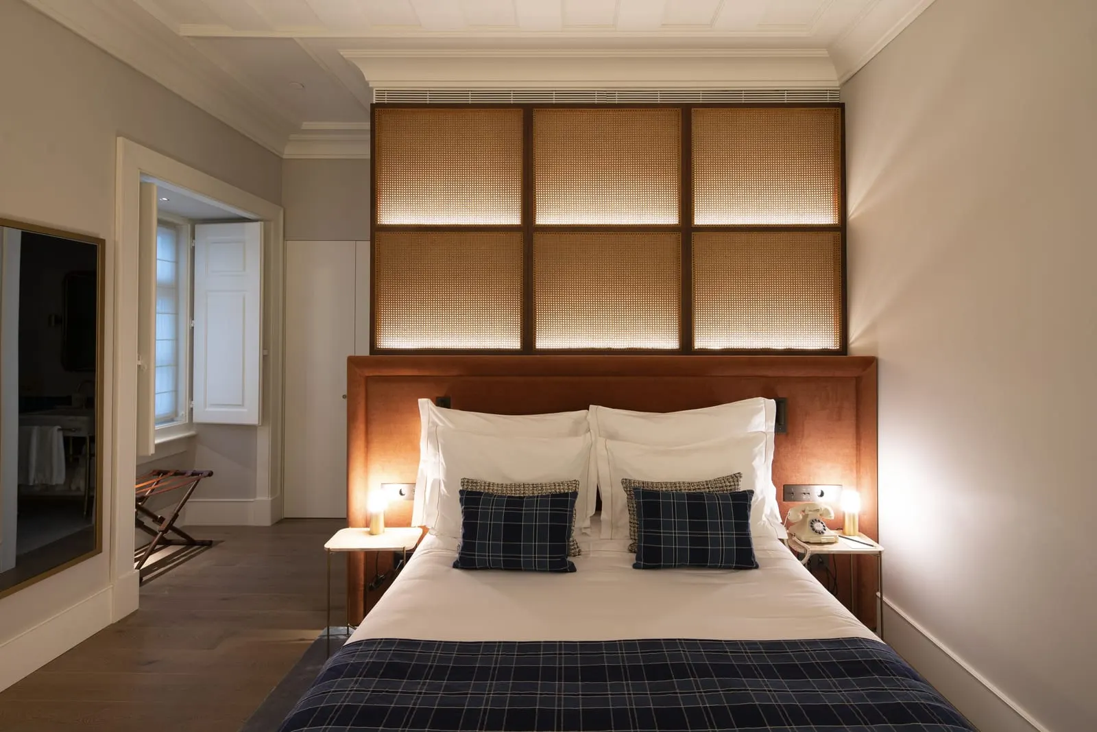 Courtyard Room at Palácio Ludovice: the bed with tartan cushions and throw beneath a lit panelled headboard