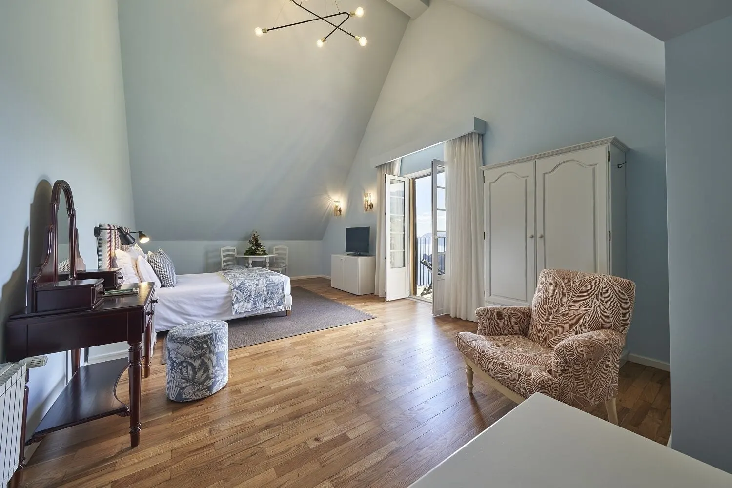 Junior Suite im Hotel Quinta do Furão: ein Doppelbett unter einer hohen schrägen Decke, ein Frisiertisch, ein Sessel, ein Holzboden und offene Glastüren zu einem Balkon