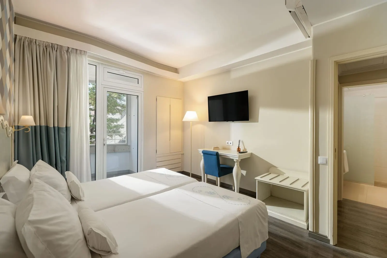 Junior Suite im Hotel Madeira: das Schlafzimmer mit einem Schreibtisch, einem Wandfernseher, einer Balkontür und einem offenen Durchgang zum Nebenraum
