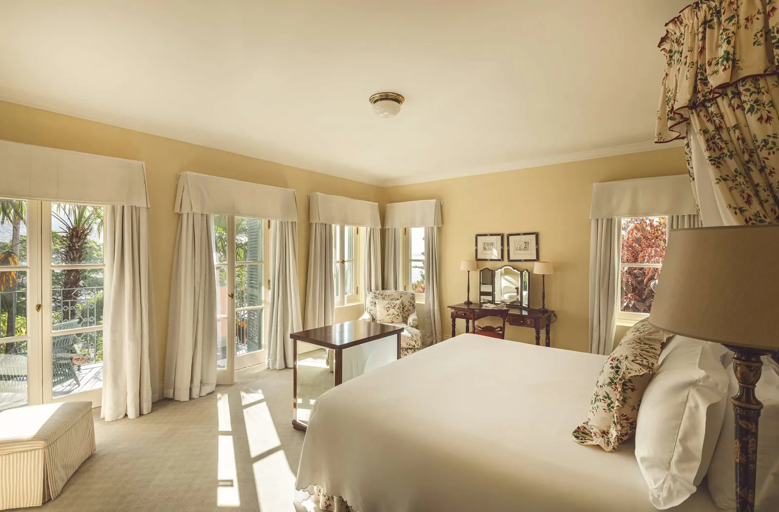 Deluxe Suite at Reid's Palace, A Belmond Hotel: a bedroom with a draped canopy over the bed and a row of tall windows and doors along two walls