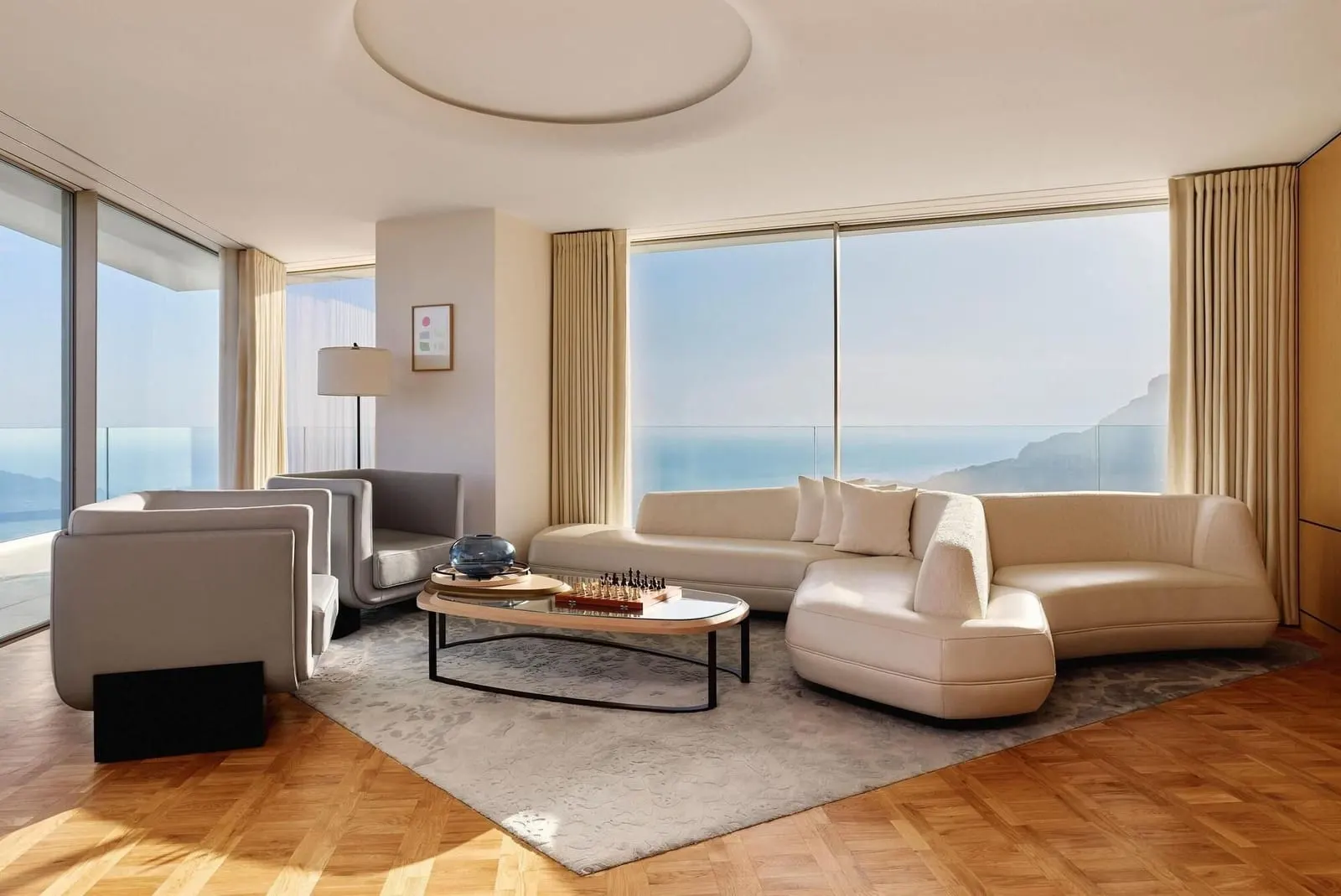 Panoramic Suite at The Maybourne Riviera: the living room with a curved sofa and windows on two sides onto the sea
