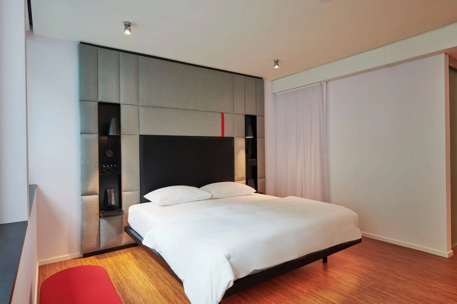 Guest Room, Accessible Guest room, 1 King at citizenM New York Bowery: a king bed on a black frame against a grey padded headboard with a black panel, a white curtain to the right and a red bench in the corner