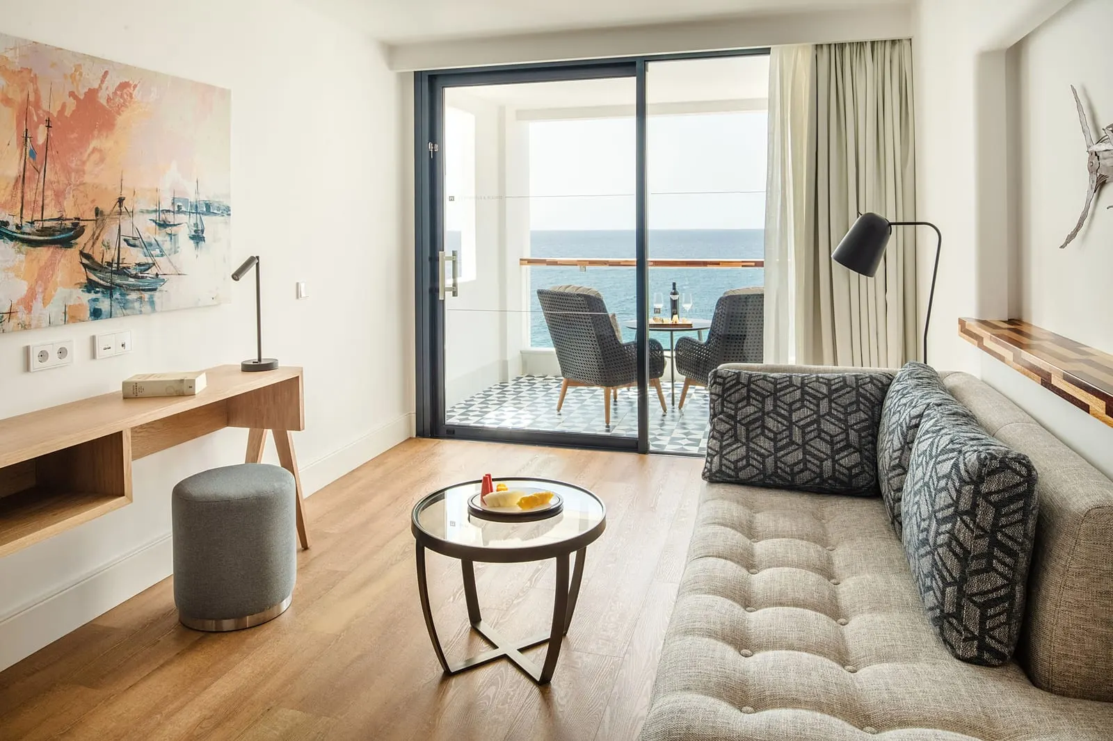 Junior Suite Sea View High Floor at Hotel Fariones: a sofa, desk and low table in front of a sliding door to a terrace with the sea beyond