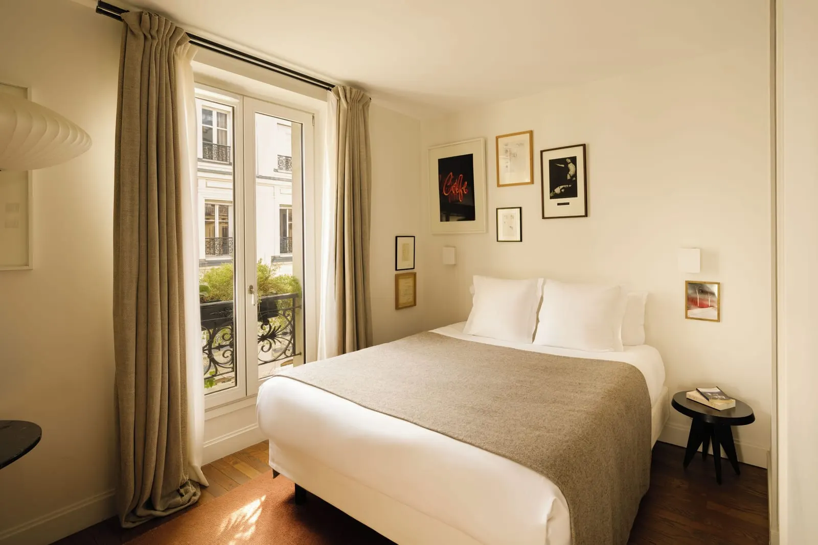 Pigalle 15 at Le Pigalle: a double bed under a cluster of framed pictures, a small round side table and a French window with a wrought-iron railing and plants
