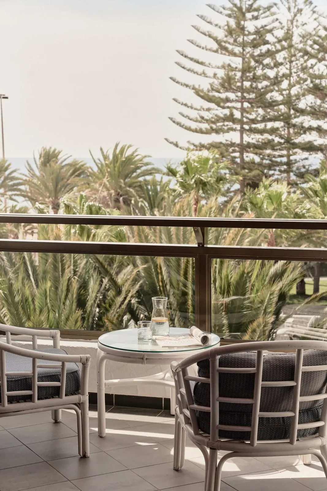 Superior Room at Seaside Palm Beach: two cane armchairs and a glass table on the balcony, above palm trees and tall pines