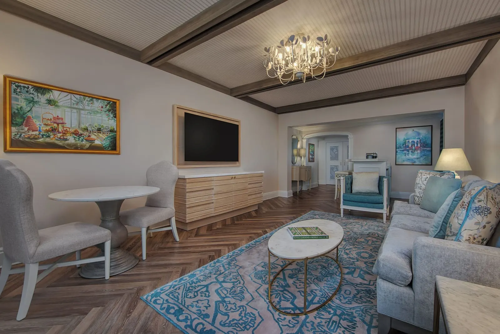 1 Bedroom Suite - Club Level Access at Disney's Grand Floridian Resort & Spa: a living room under a beamed ceiling with a sofa, an armchair, an oval marble coffee table, a round table with two chairs and a wall-mounted television