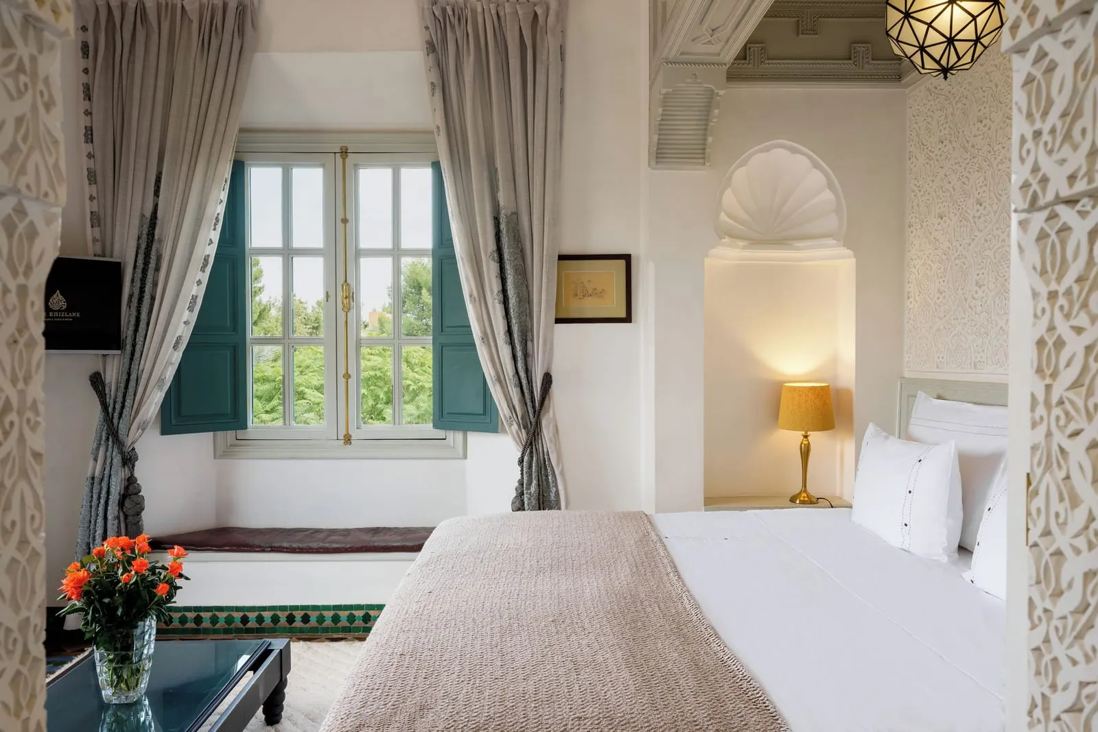 Orient Suite at Dar Rhizlane: a double bed beside a shell-carved alcove, with a cushioned window seat under a tall shuttered window