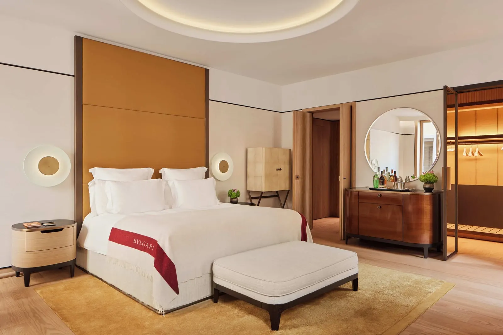 Junior Suite at Bvlgari Hotel Roma: a double bed with a branded throw, a bench at its foot and a round mirror over a cabinet