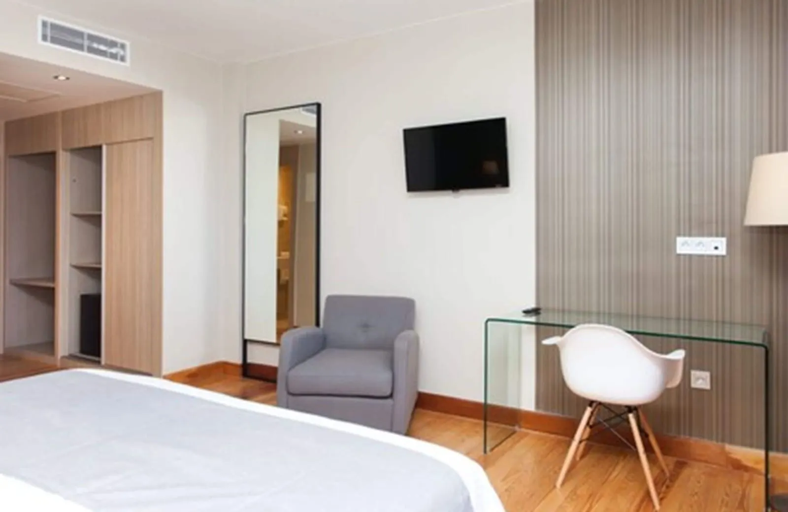 Double Room at El Mirador de Fuerteventura: the foot of the bed facing open wardrobes, a long mirror, an armchair, a glass desk and a wall television