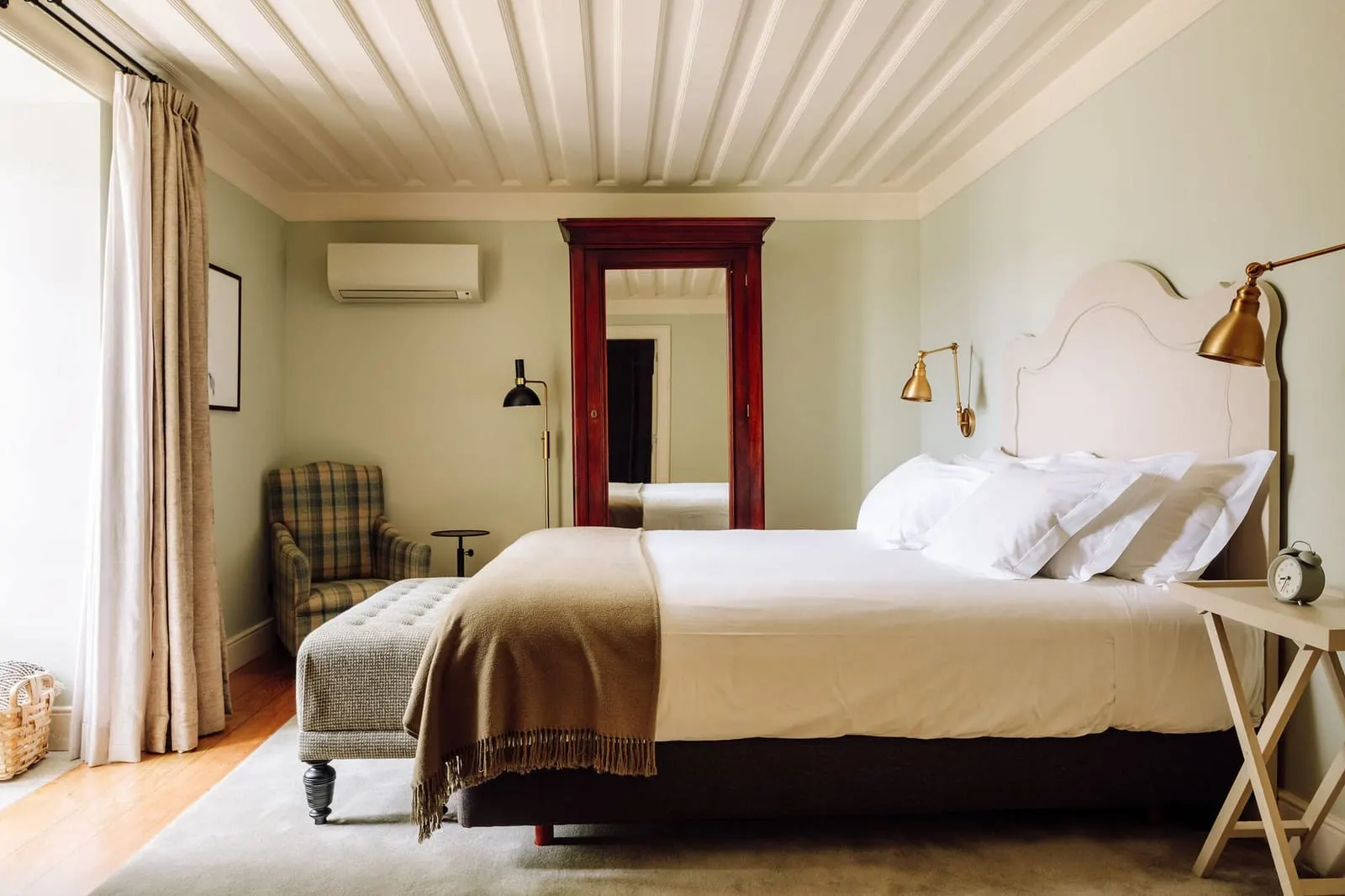Premium Manor House Accommodation at Quinta Nova: a bed with a white arched headboard, a tall framed mirror and an armchair
