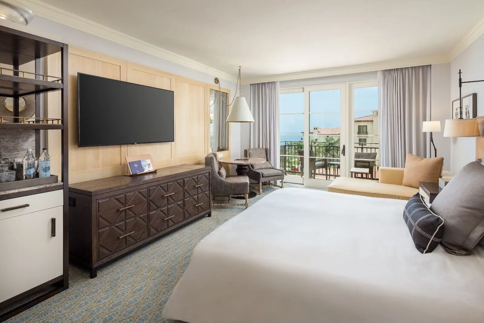 Hotel King Guestroom, Ocean View at Terranea Resort: a king bed facing a wall-mounted television above a carved wooden console, with a small seating area and glass doors onto a balcony