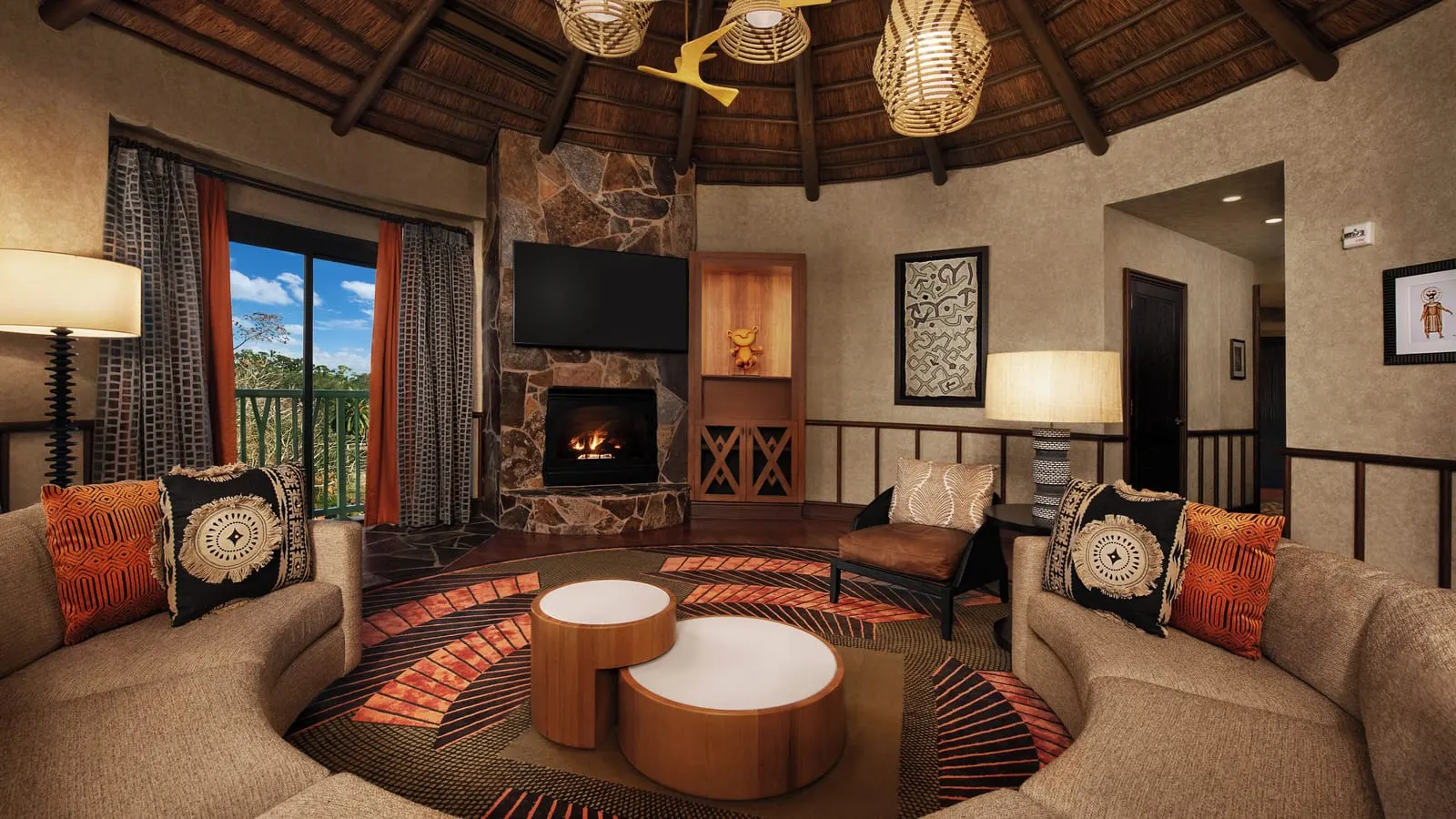 Royal Kuba VP Club Level Suite at Disney's Animal Kingdom Lodge: the round living room under a thatched ceiling, with curved sofas, a stone fireplace with a television above it and a door onto the balcony