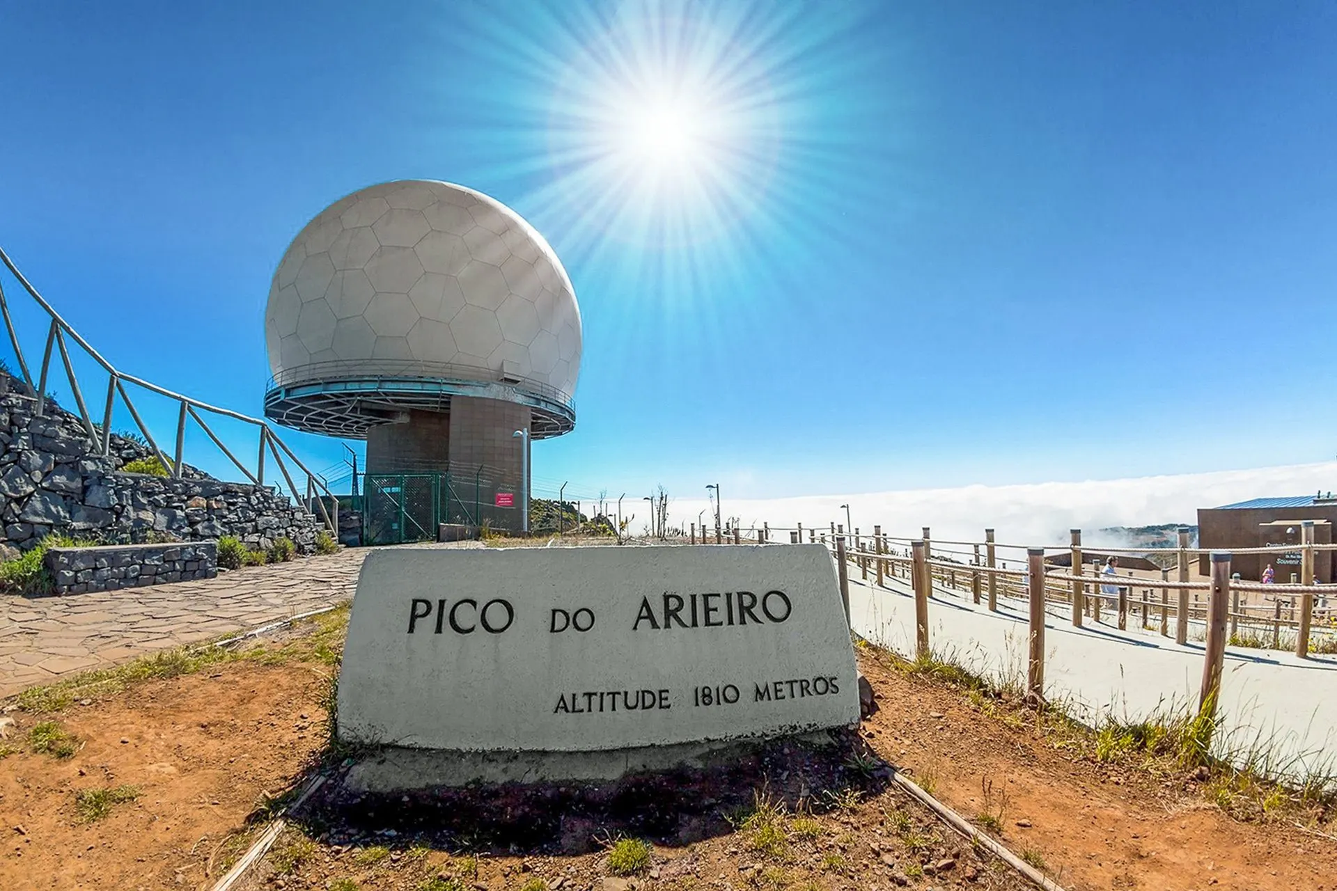 The stone marker on the summit of Pico do Arieiro with the white radar dome behind it and a sea of cloud below the railings