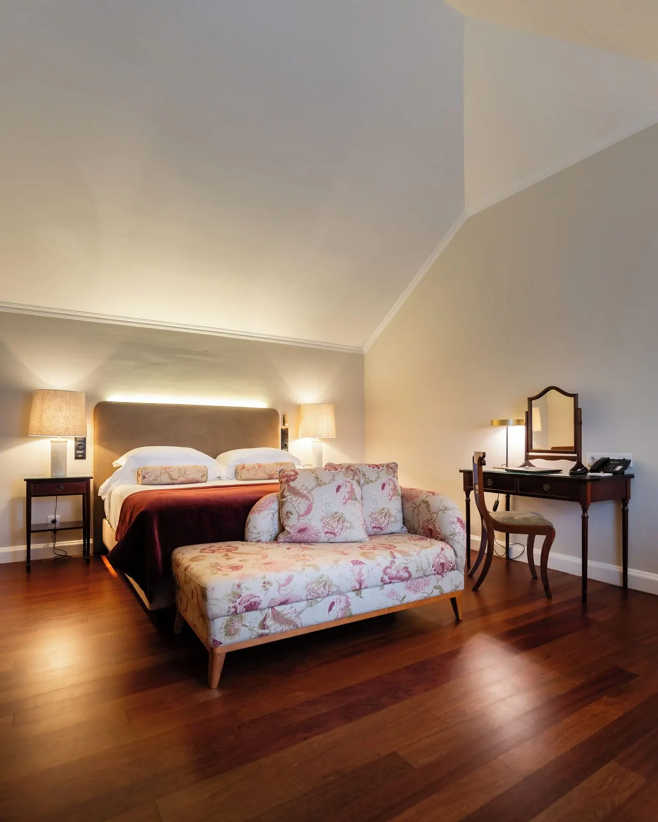 Double Main House at Casa Velha do Palheiro, Relais & Châteaux: a double bed under a sloping ceiling, a floral settee at its foot and a dressing table