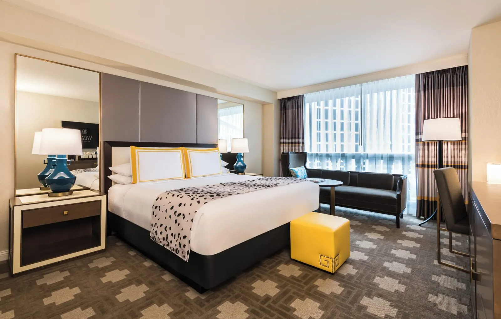 Julius Strip View Room im Caesars Palace: ein Kingsize-Bett mit blauen Lampen und einem gelben Polsterhocker, ein Schreibtisch und ein Sofa am Fenster