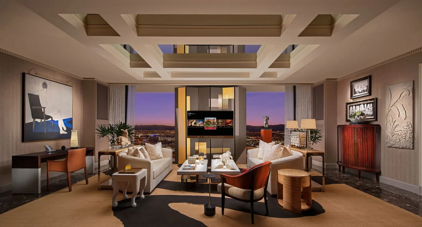 Wynn Tower Suite Salon at Wynn Las Vegas: the living room, with two cream sofas facing each other across low white tables, a red armchair, a desk and a television on a black and gold screen between two windows