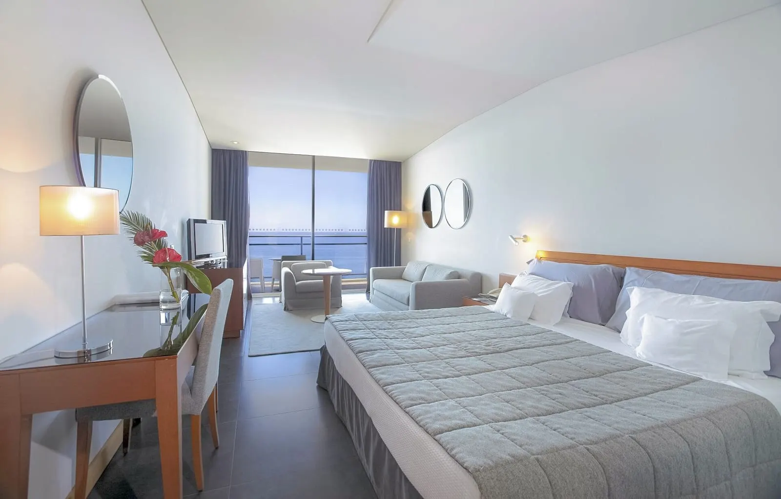 Superior Sea View at VidaMar Resort Hotel Madeira: a large bed, a desk, a sofa and an armchair, with a glass wall to the balcony and the sea beyond