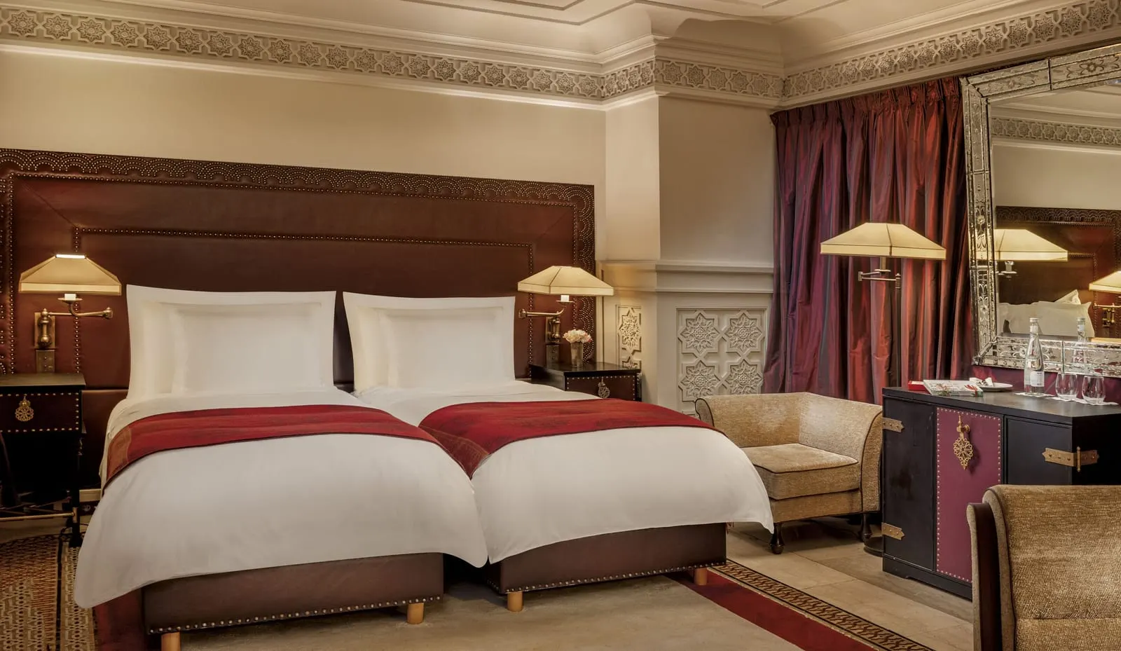 Classic Room at La Mamounia: twin beds with red throws under a leather headboard, an armchair and a cabinet beside long red curtains