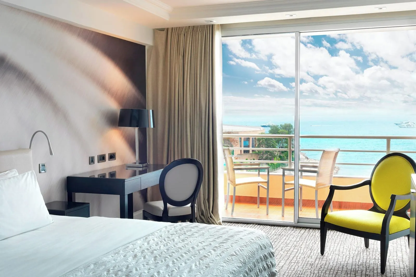 Deluxe sea-view room at Le Méridien Beach Plaza: a desk and a yellow armchair by glass doors to the balcony and the sea