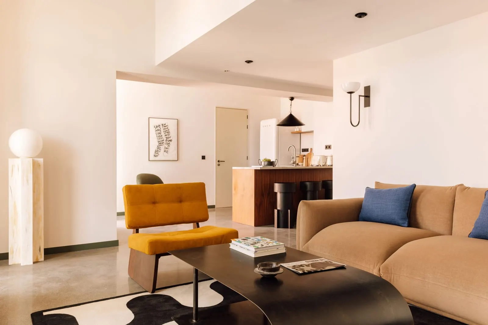 Two Bedroom Duplex Suite at The Rebello: the living room with a sofa and a yellow armchair, and the kitchen island beyond