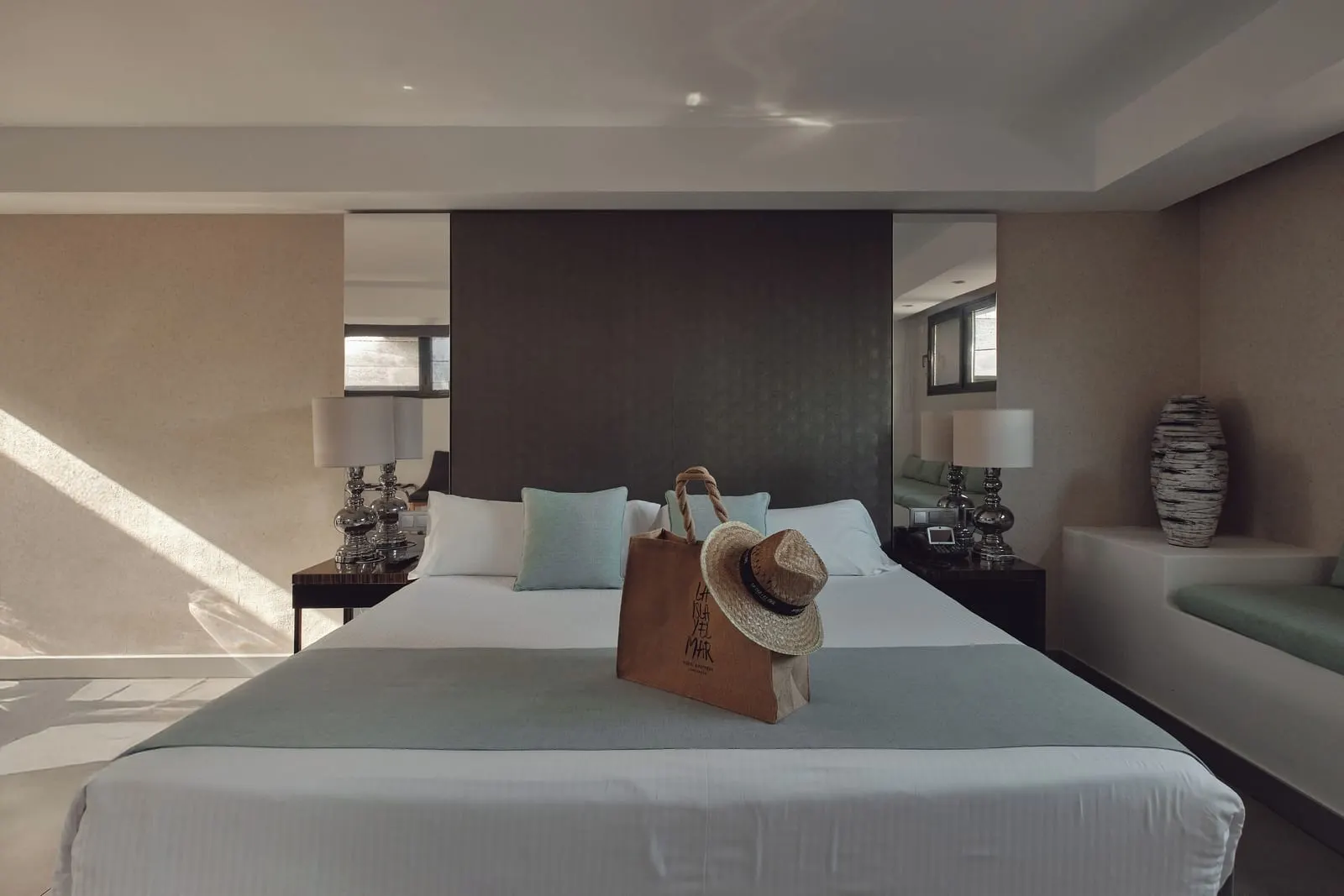 Premium Suite at La Isla y el Mar Hotel Boutique: a king bed with a straw bag and hat on it, against a dark panelled wall