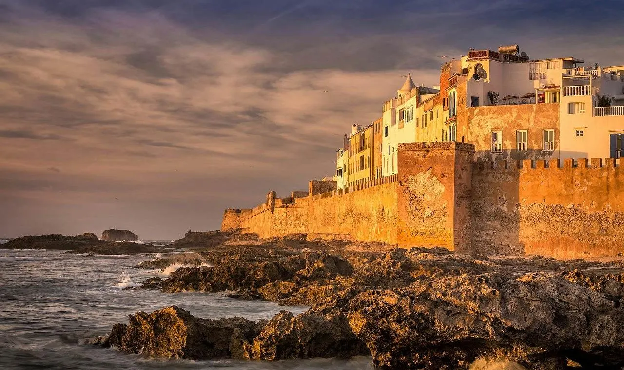 Essaouira's crenellated sea walls and white houses lit by low sun above dark rocks and Atlantic surf