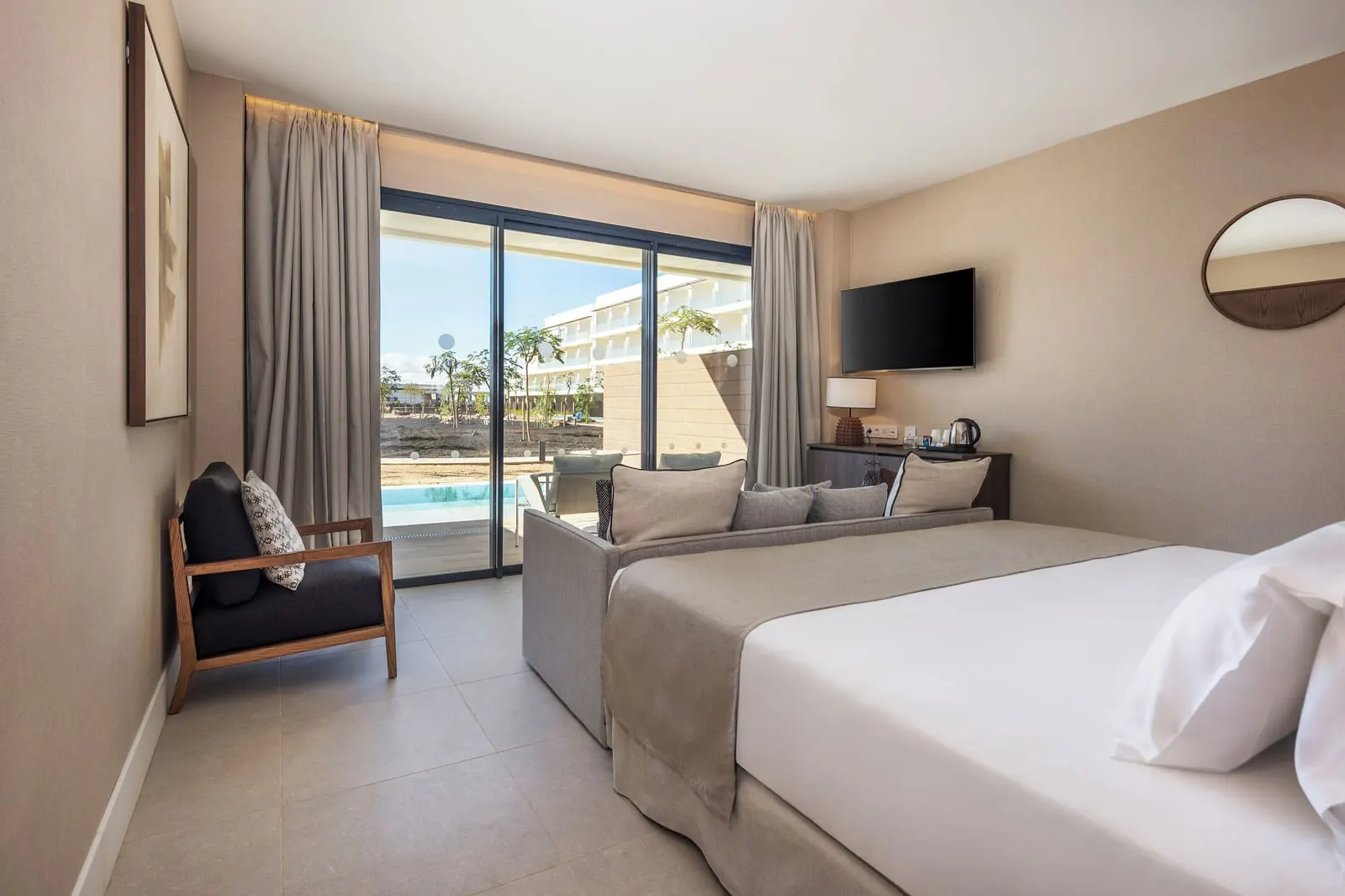 Superior Swim Up at Barceló Playa Blanca: a bed and sofa in front of a glass door that opens towards the pool