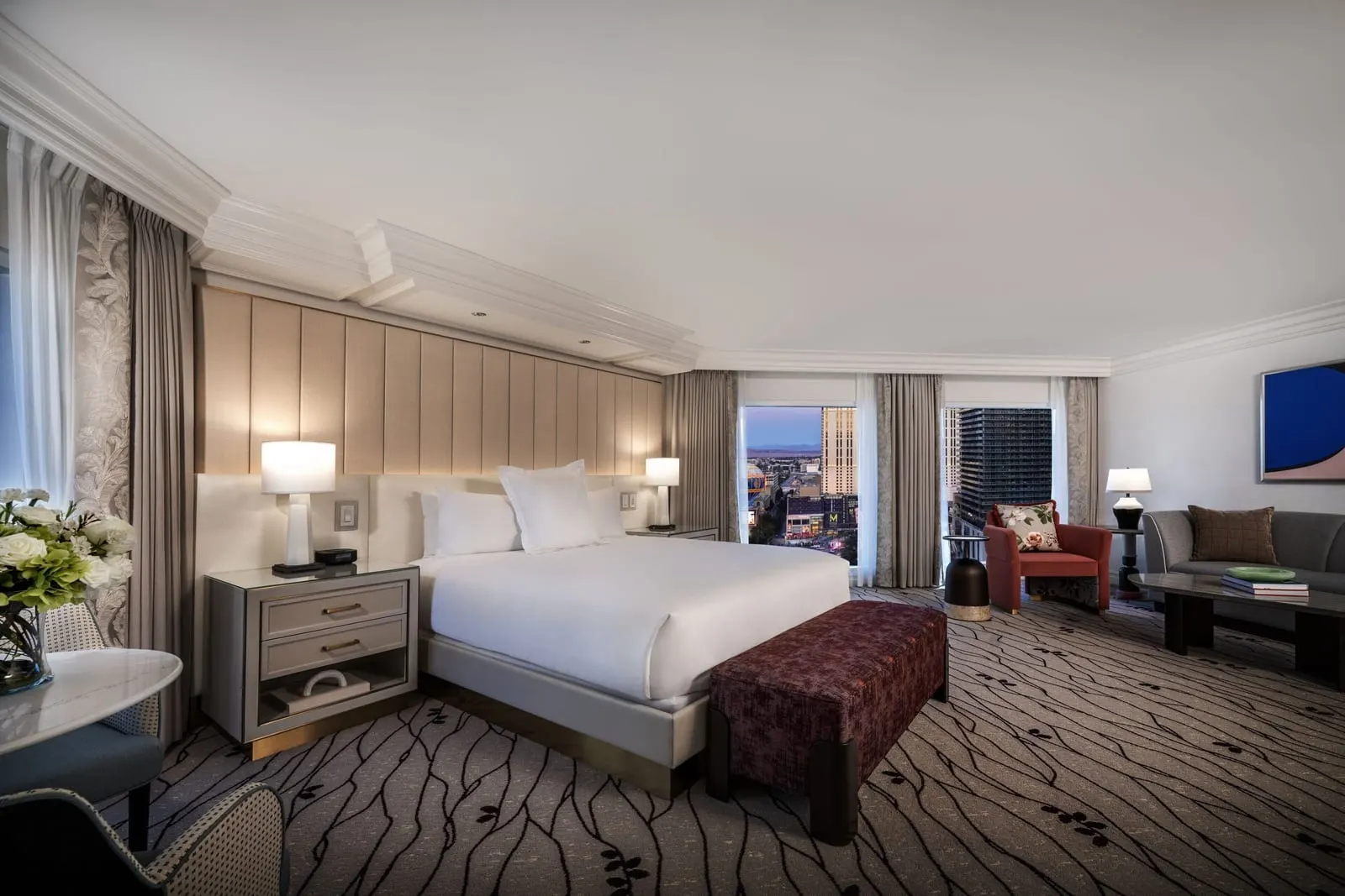 Salone Suite at Bellagio: a king bed with a tall padded headboard and, beyond it, a sitting area with a sofa, a red armchair and a coffee table