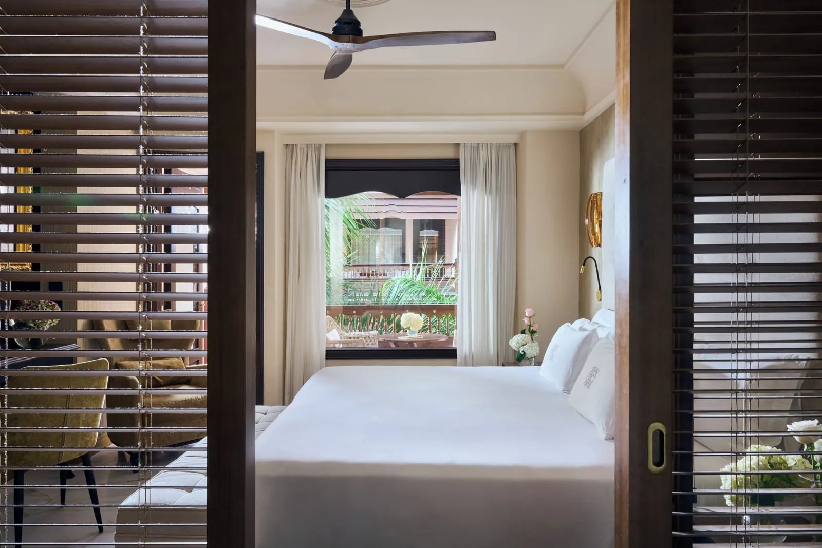 Deluxe Superior at Santa Catalina, a Royal Hideaway Hotel: a double bed seen through slatted wooden sliding doors, under a ceiling fan, with a window on to a furnished balcony