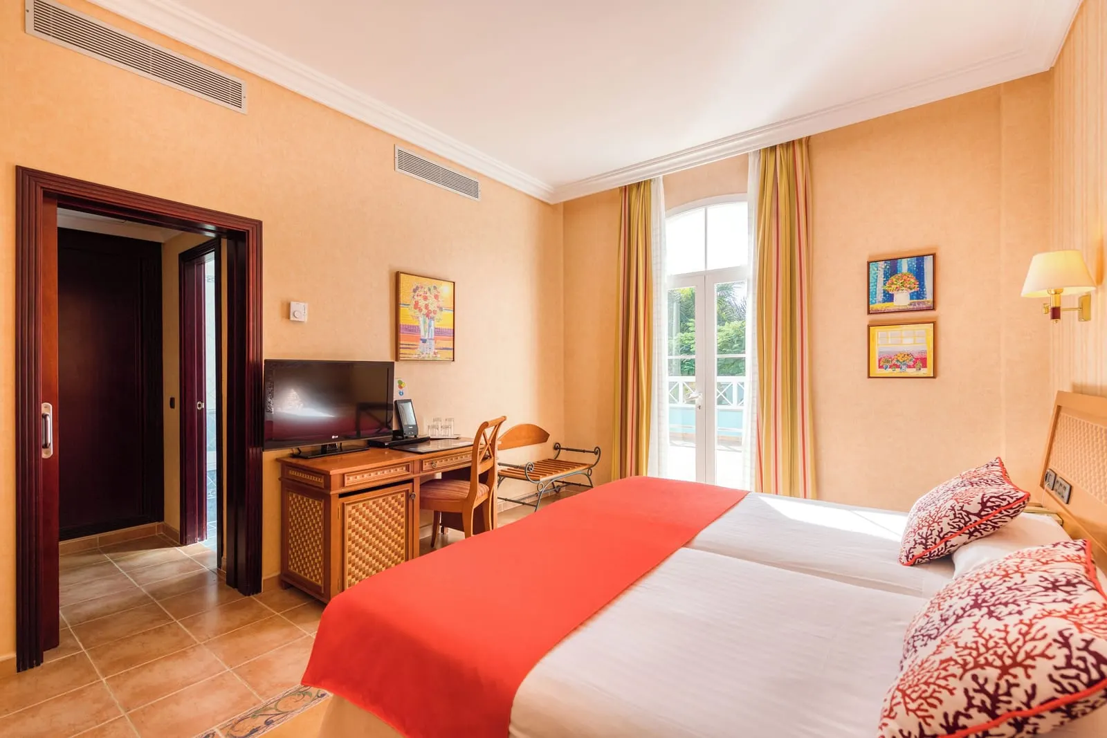 Superior Room at Hotel Cordial Mogán Playa: two single beds side by side, a desk with a television, a luggage rack and arched glass doors at the far end