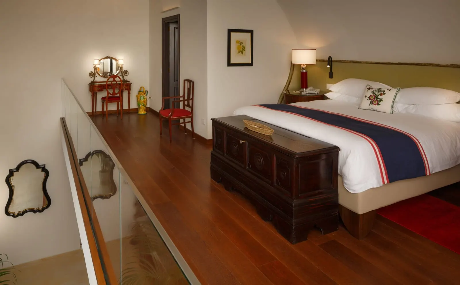 Rosa Suite at Monastero Santa Rosa: a king bed with a wooden chest at its foot on a wood-floored upper level behind a glass balustrade.