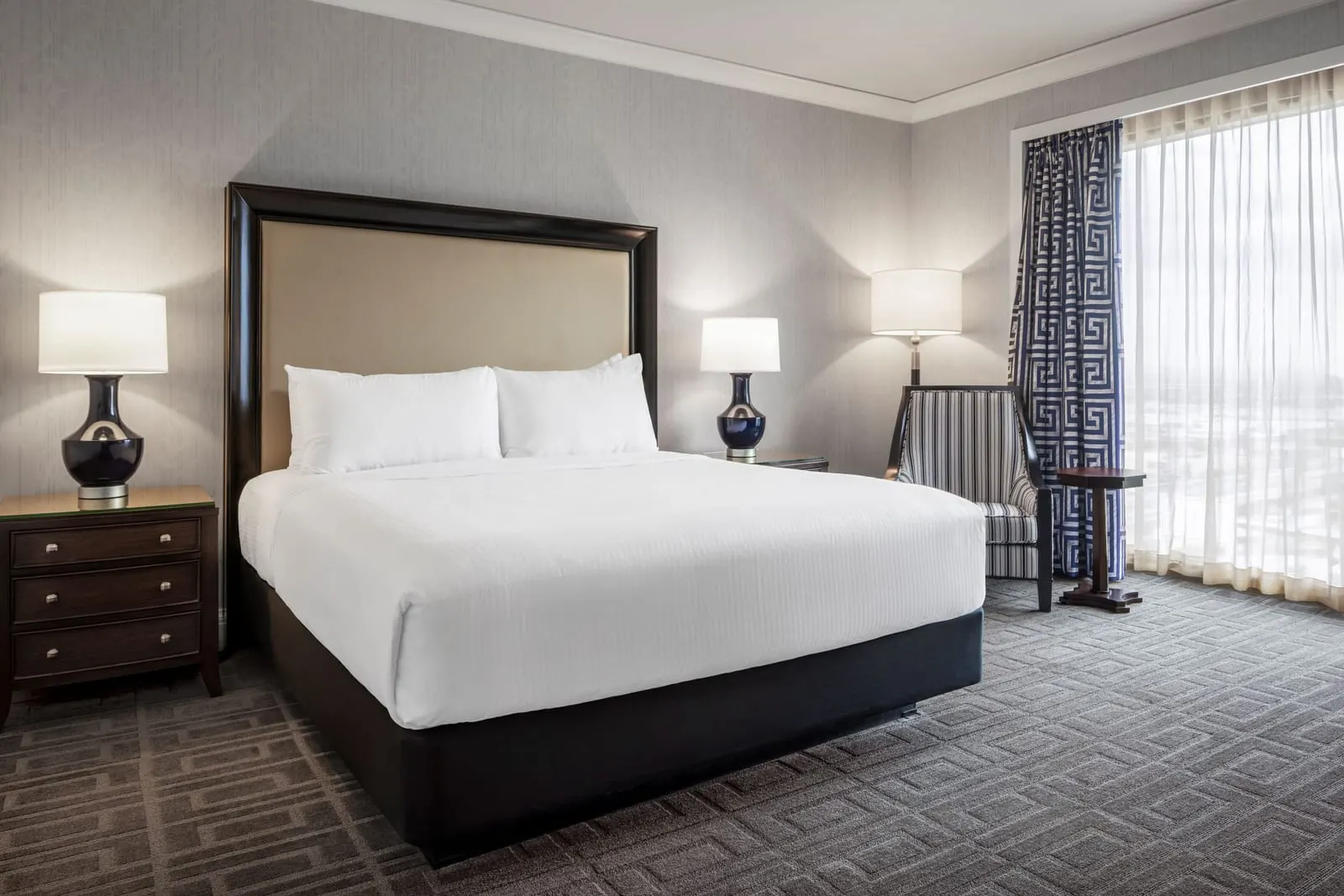 Palace Premium Room im Caesars Palace: ein Kingsize-Bett mit dunklen Lampen, ein gestreifter Sessel und ein Beistelltisch an einem Fenster mit Gardinen