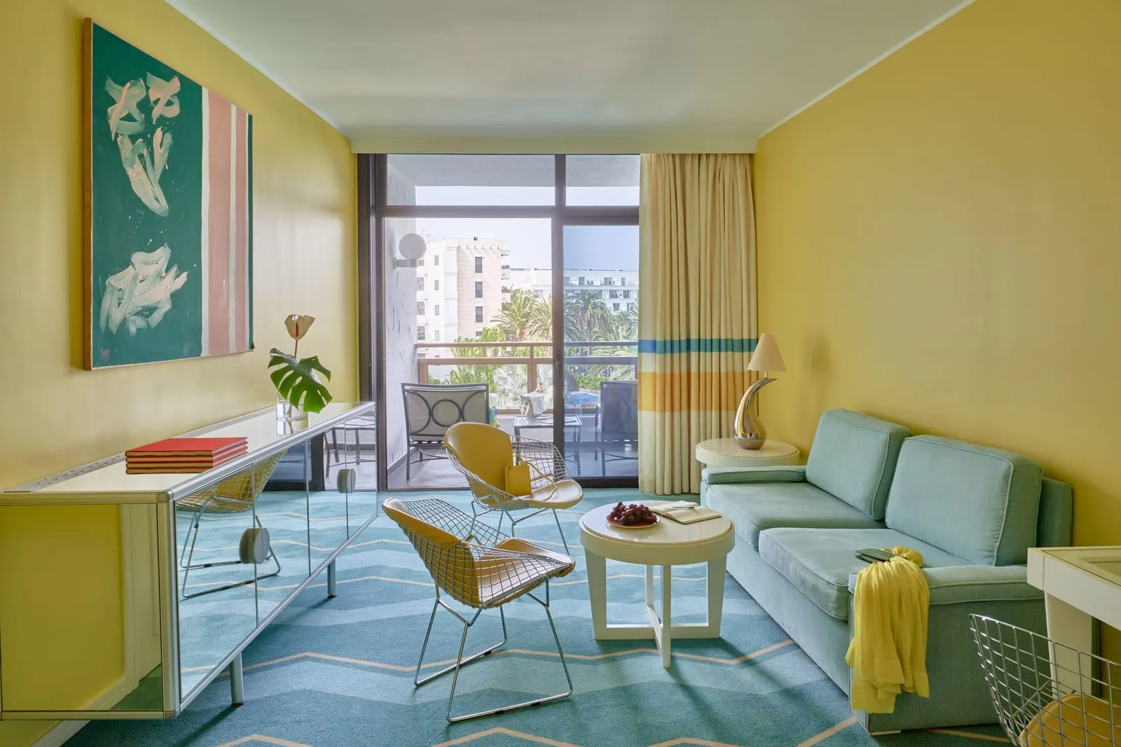 Junior Suite at Seaside Palm Beach: the lounge area, with yellow walls, a pale blue sofa, wire chairs and a glass door to the balcony