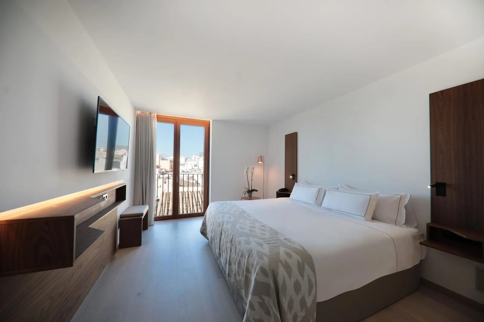 Junior Suite at Es Princep: a double bed facing a wall-mounted television, with a balcony door onto the rooftops of the old town