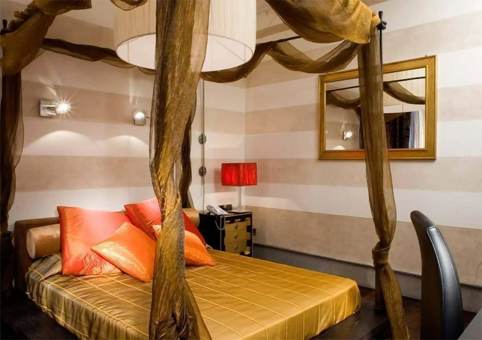 Deluxe Double Room at The Inn at the Roman Forum: a canopy bed with gauze drapes, orange cushions and striped walls