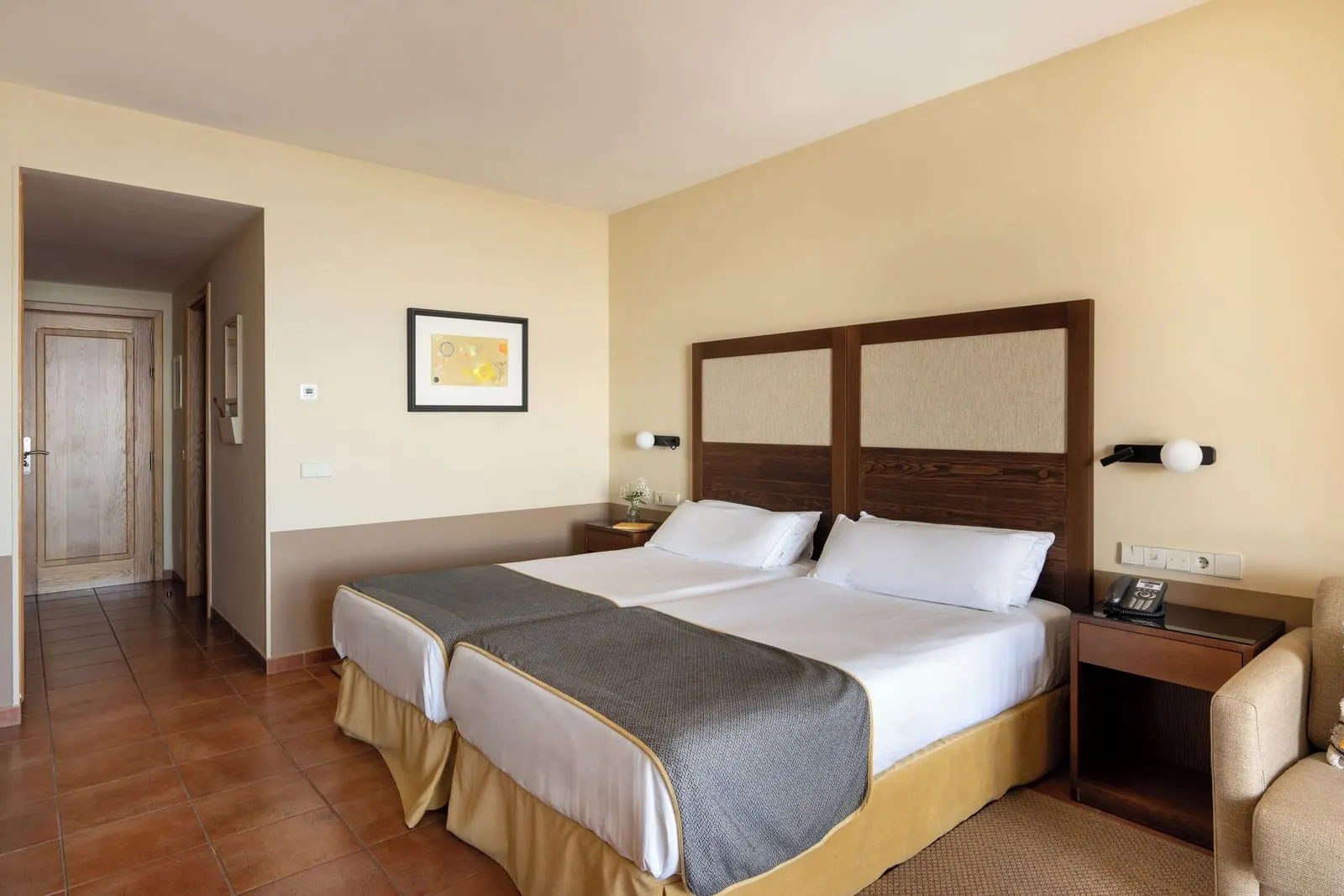 Standard Double at Parador de Cruz de Tejeda: two single beds side by side under a wood and linen headboard, with a terracotta tiled floor and a short hall to the door