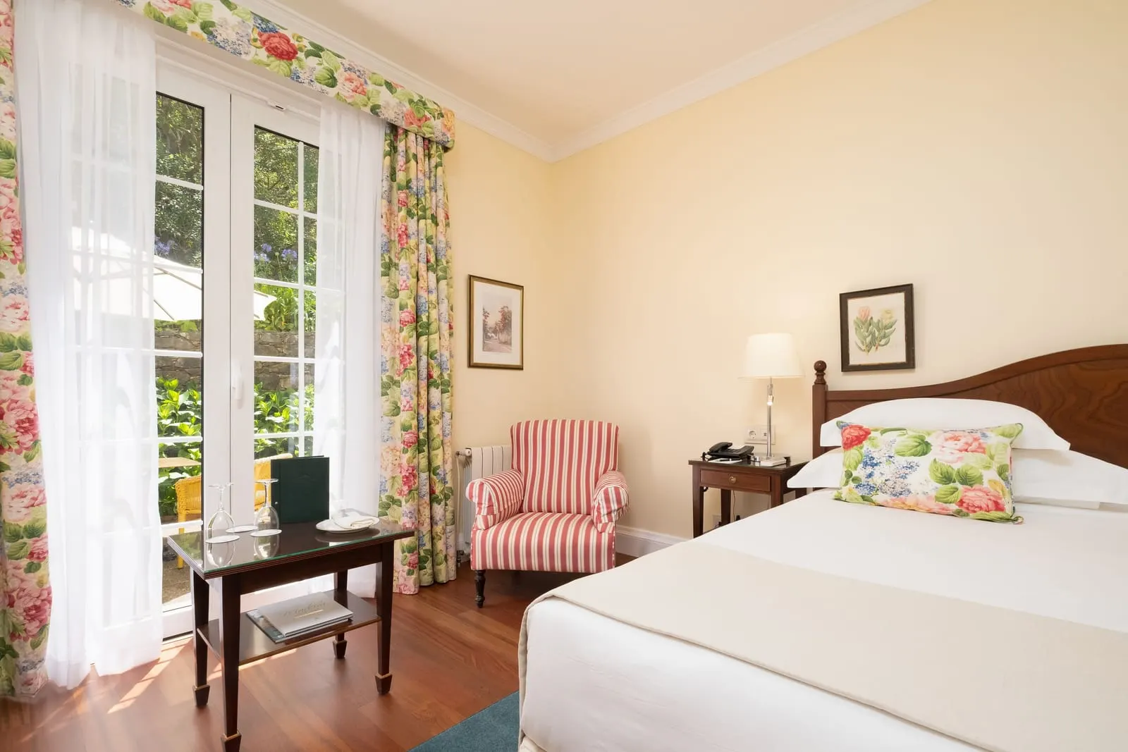 Double Golf Wing at Casa Velha do Palheiro, Relais & Châteaux: a striped armchair, a side table and a wooden floor by tall glazed doors to the patio