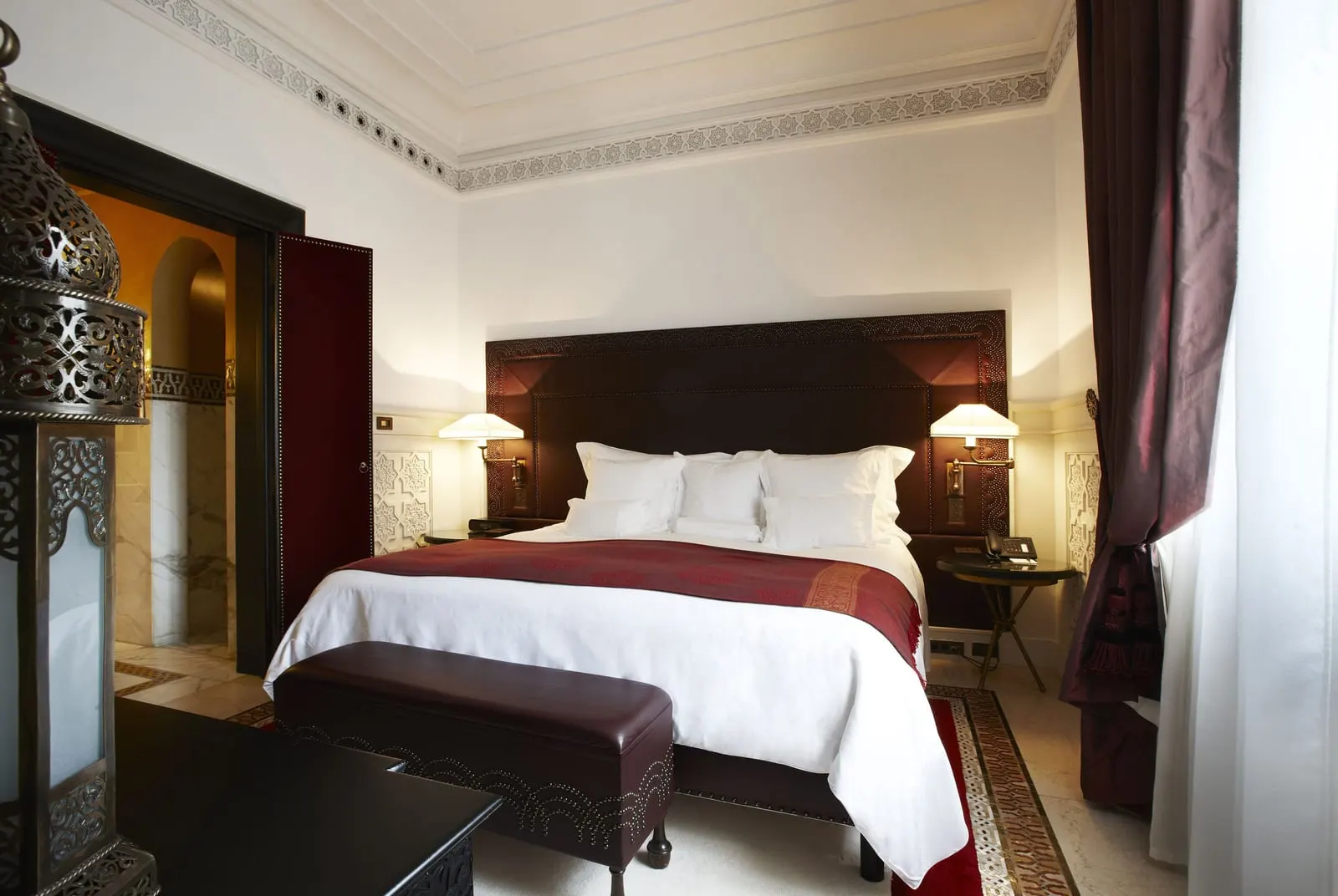 Park Suite at La Mamounia: a king bed with a red throw and a dark headboard, a leather bench and a carved lantern