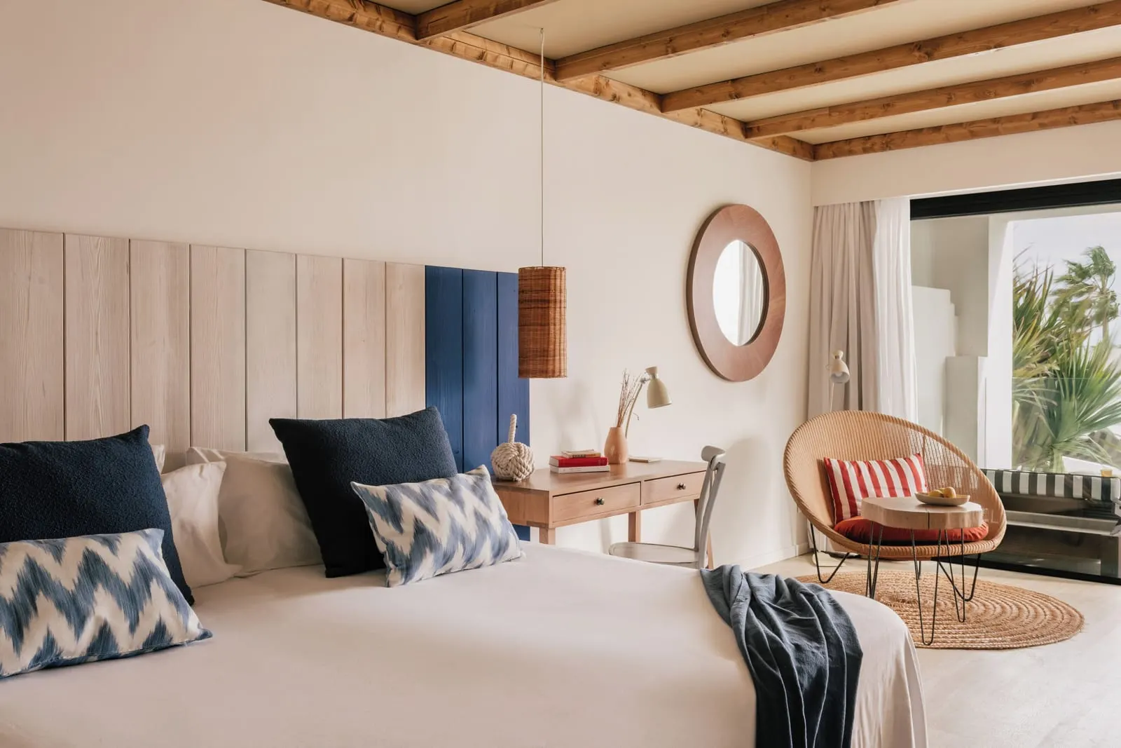 Zel Room at ZEL Fuerteventura: a double bed with blue and white cushions, a wooden desk and a wicker armchair by a glass door to the balcony