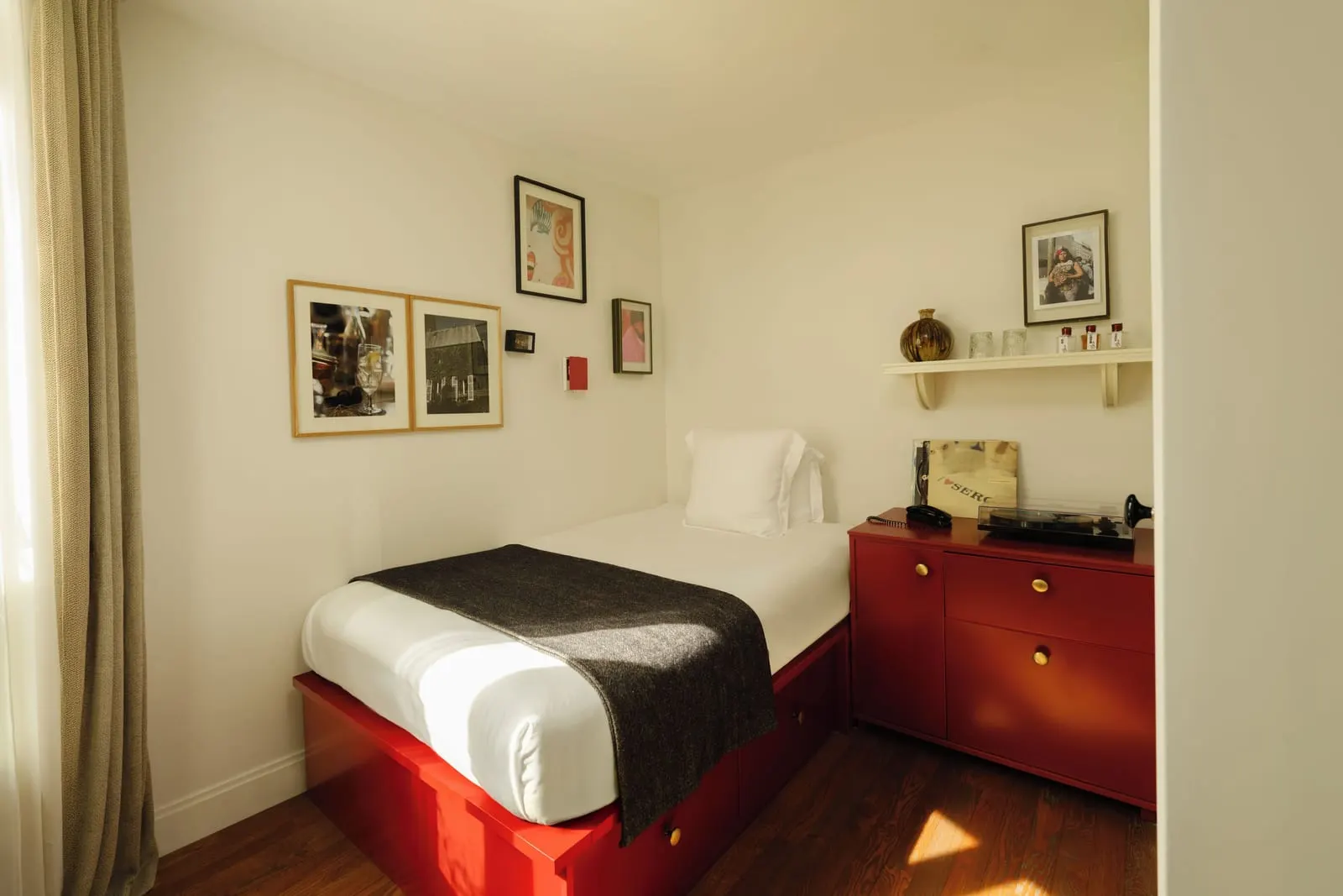 Pigalle 12 at Le Pigalle: a single bed on a red base with drawers, beside a red cabinet holding a turntable, records and a telephone, under framed pictures and a small wall shelf